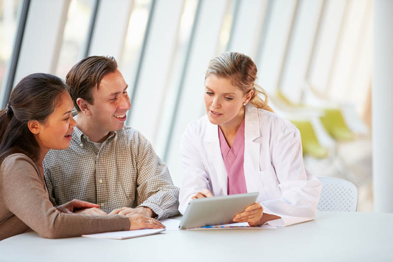 Female Doctor Using Digital Tablet Talking With Patients